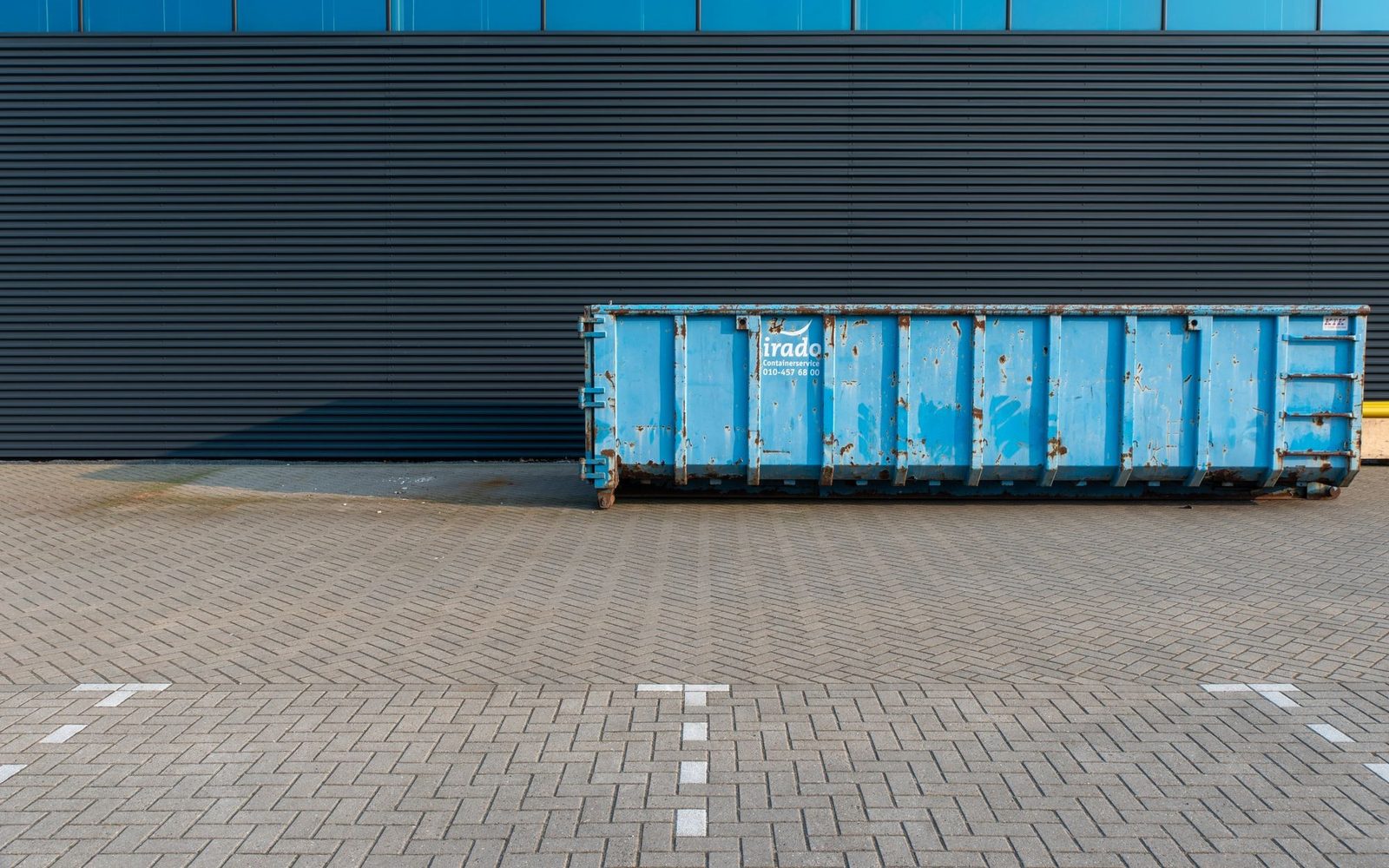 Large blue roll-on waste container standing outside a commercial building