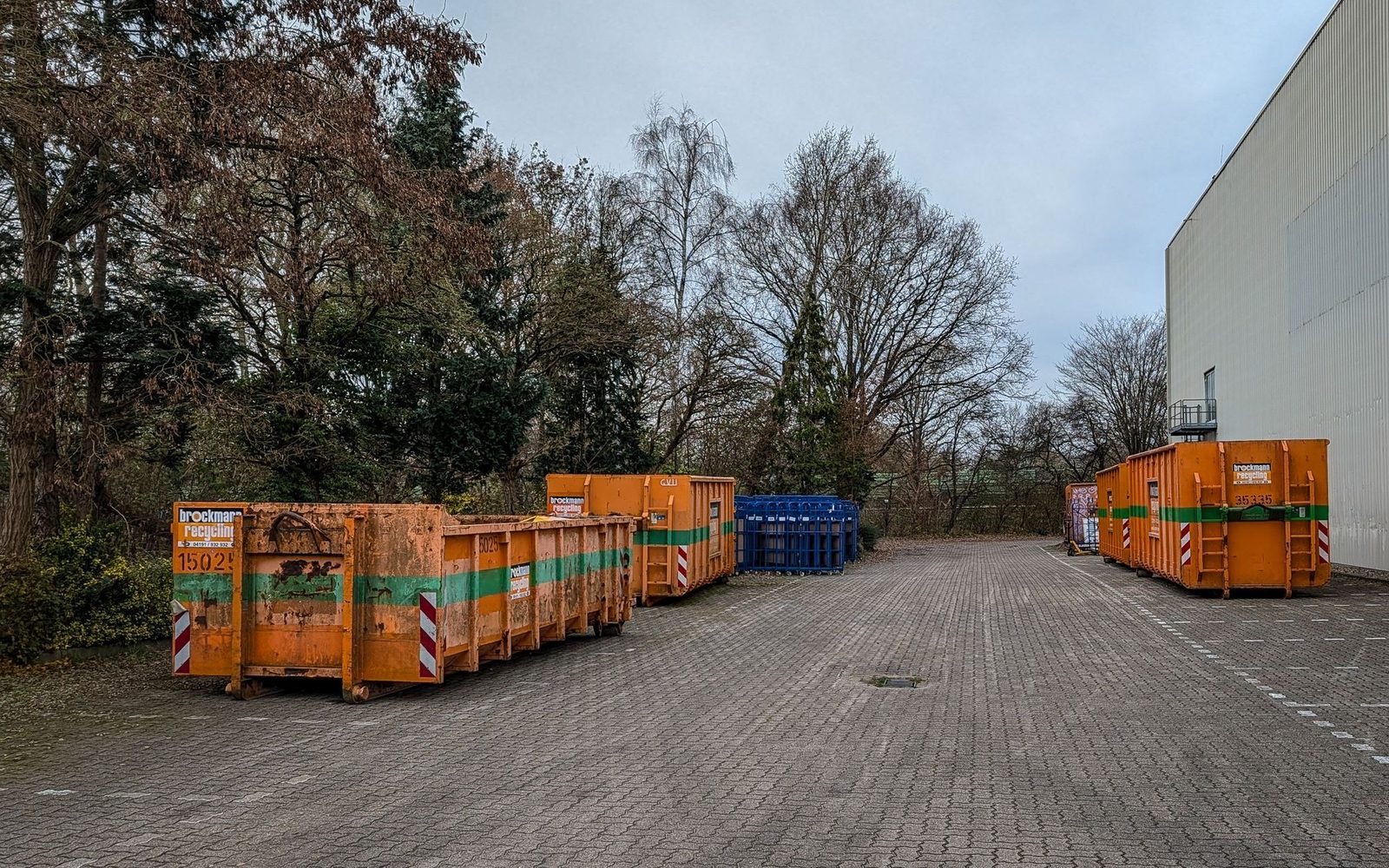 Row of large open waste containers parked on a paved yard