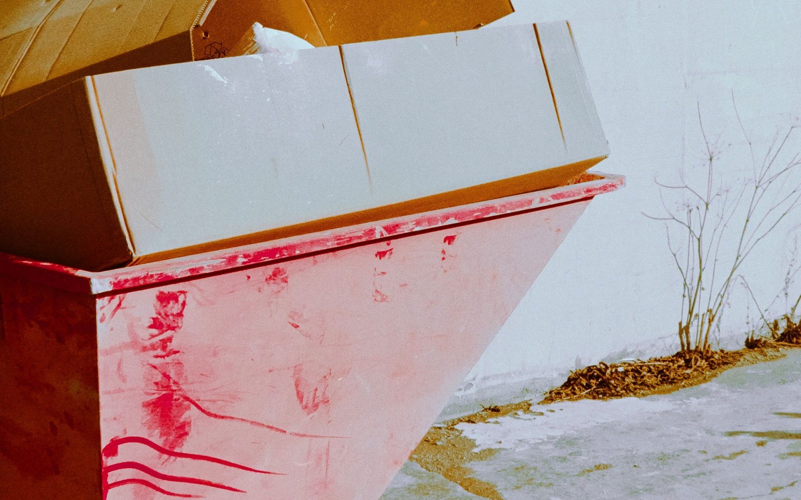 Small red skip filled with flattened cardboard beside a wall
